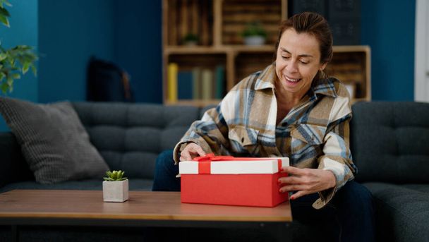 Mulher hispânica de meia idade unboxing presente sentado no sofá em casa - Foto, Imagem