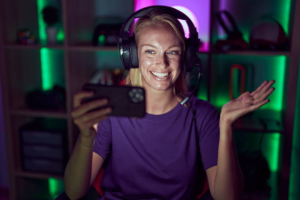 Junge Spielerin bei Videospielen mit Smartphone feiert Leistung mit glücklichem Lächeln und Siegerausdruck mit erhobener Hand  - Foto, Bild