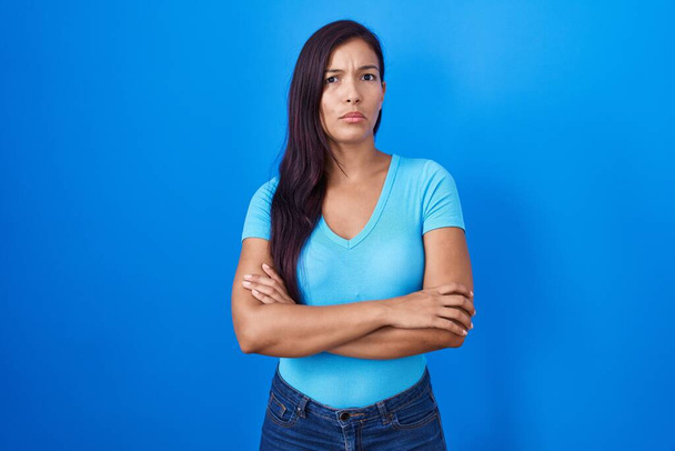 Young hispanic woman standing over blue background skeptic and nervous, disapproving expression on face with crossed arms. negative person.  - Foto, imagen