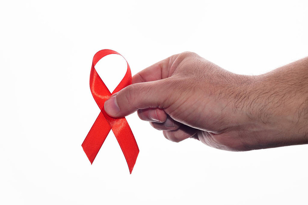 Το χέρι ενός άνδρα που κρατάει μια κόκκινη κορδέλα για να υποστηρίξει την Παγκόσμια Ημέρα κατά του AIDS σε λευκό φόντο. 1η Δεκεμβρίου, ημέρα hiv - Φωτογραφία, εικόνα