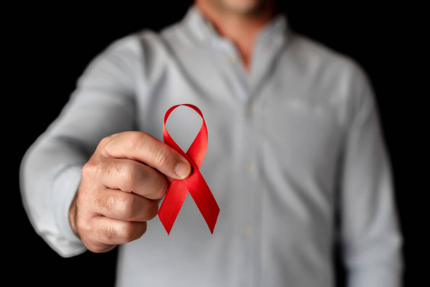 Een man toont de camera een rood lint ter ondersteuning van Wereld Aids Dag op een zwarte achtergrond. Bestrijding van het hiv-virus - Foto, afbeelding