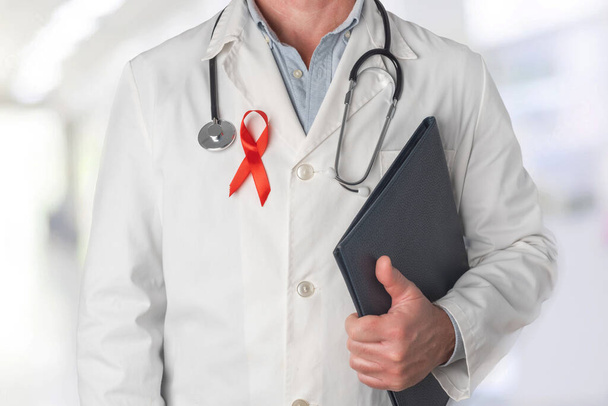 Docteur tenant un dossier avec des rapports médicaux et portant un ruban rouge sur sa poitrine, symbole de la Journée mondiale du sida. Soutien du personnel de santé aux personnes atteintes du VIH. Prévention et lutte contre le virus du sida - Photo, image