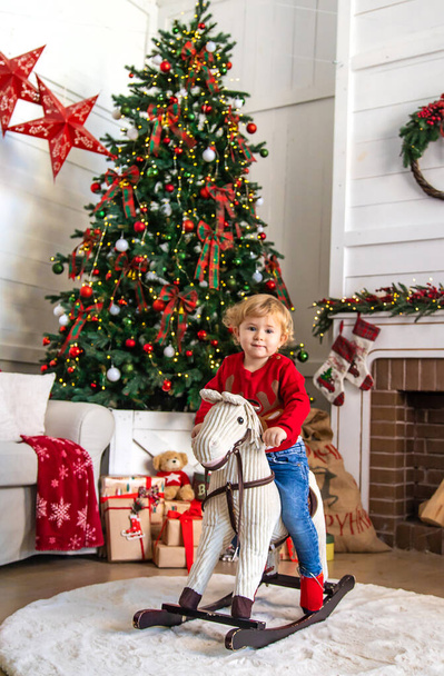 Kind te paard bij de kerstboom. Selectieve focus. Jongen. - Foto, afbeelding