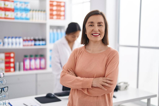 Dos mujeres farmacéuticas y cliente sonriendo confiadas en la farmacia - Foto, Imagen