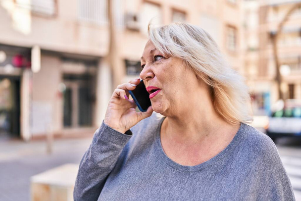 Middle age blonde woman talking on the smartphone at street - Photo, Image