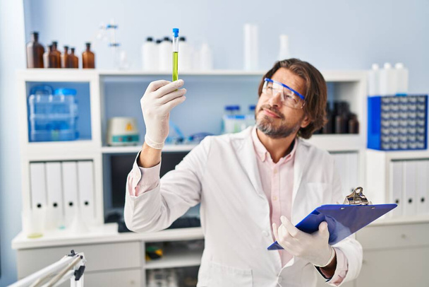 Middle age man scientist looking test tube holding clipboard at laboratory - Photo, Image
