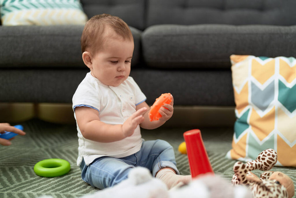 Liebenswertes Kleinkind spielt mit Spielzeug, das zu Hause auf dem Boden sitzt - Foto, Bild
