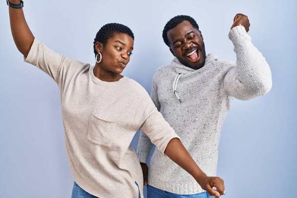 Young african american couple standing over blue background together dancing happy and cheerful, smiling moving casual and confident listening to music  - Foto, immagini