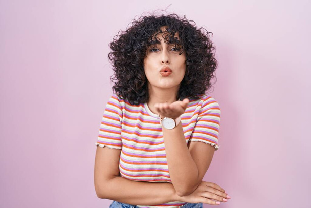 Young middle east woman standing over pink background looking at the camera blowing a kiss with hand on air being lovely and sexy. love expression.  - Photo, Image