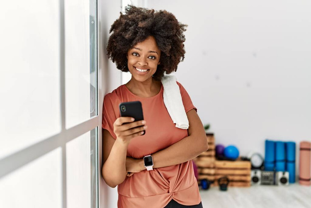 Jonge Afrikaanse Amerikaanse vrouw lacht vol vertrouwen met behulp van smartphone bij sportcentrum - Foto, afbeelding