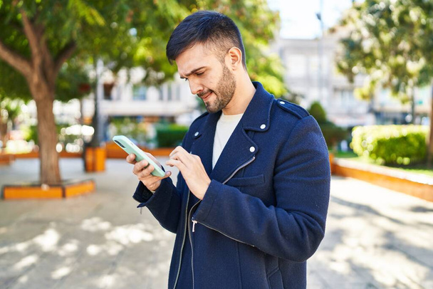 Young hispanic man using smartphone with serious expression at park - Photo, Image