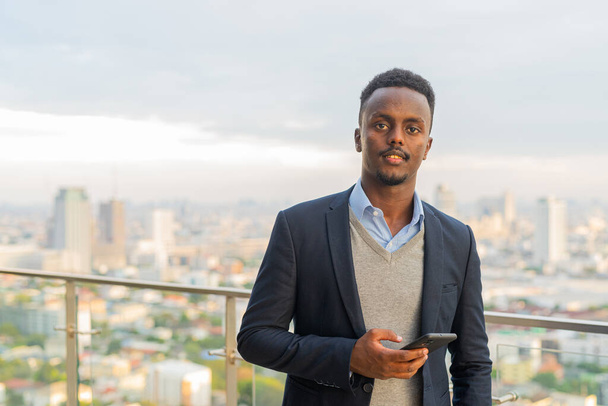Portrait of handsome black African businessman wearing suit and holding smart phone - Foto, imagen