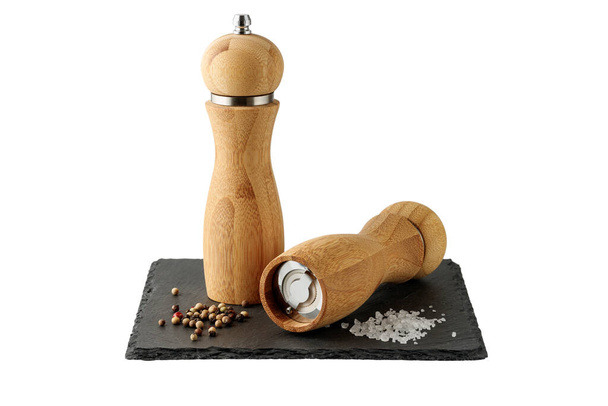 Wooden salt and peppers mill on black slate board isolated on white background. Two bamboo spice grinders.  - Photo, Image