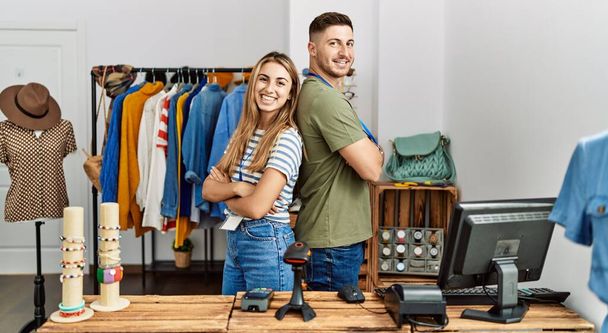 Двое латиноамериканцев улыбаются счастливо стоя со скрещенными руками в магазине одежды. - Фото, изображение