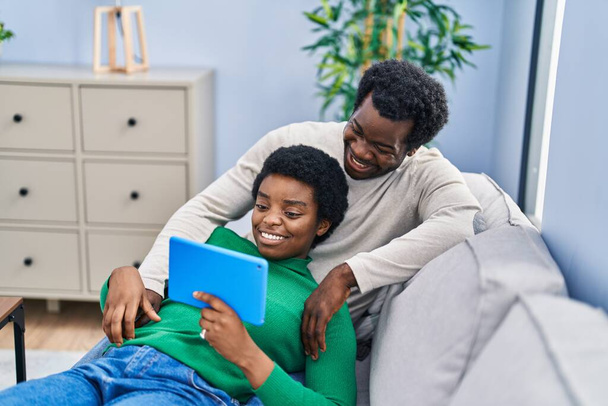 Afrikaans amerikaans man en vrouw paar met behulp van touchpad zitten op de bank thuis - Foto, afbeelding