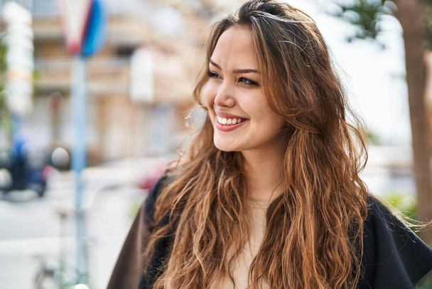 Νεαρή όμορφη ισπανόφωνη γυναίκα χαμογελά με αυτοπεποίθηση κοιτάζοντας στο πλάι στο δρόμο - Φωτογραφία, εικόνα