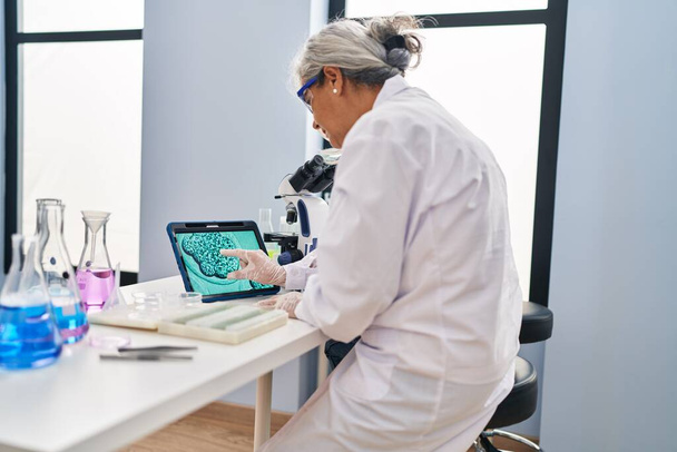 Middle age woman wearing scientist uniform watching embryo on touchpad at laboratory - Foto, immagini