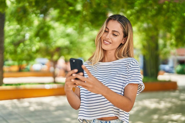 Jovem loira sorrindo confiante usando smartphone no parque - Foto, Imagem