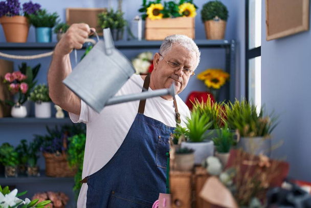 Middle age grey-haired man florist watering plant at florist - Foto, Bild