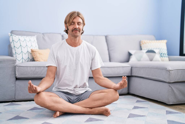 Mladý blonďatý muž se usmívá sebevědomý trénink jóga doma - Fotografie, Obrázek