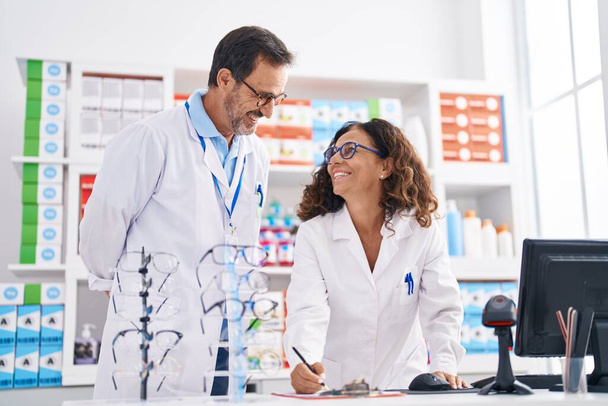 Чоловік і жінка фармацевти пишуть на документі, що працює в аптеці
 - Фото, зображення