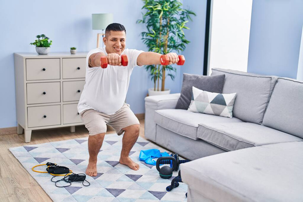 Jovem latino homem treinamento perna exercício usando halteres em casa - Foto, Imagem