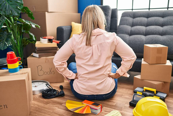 Young hispanic woman moving to a new home sitting on the floor standing backwards looking away with arms on body  - Photo, image