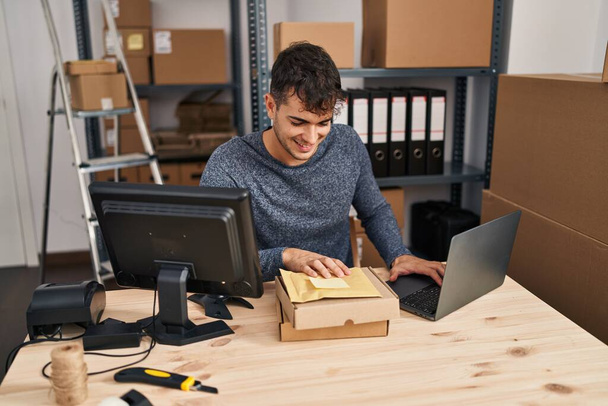 Joven hombre hispano comercio electrónico trabajador de negocios utilizando paquetes portátiles en la oficina - Foto, Imagen