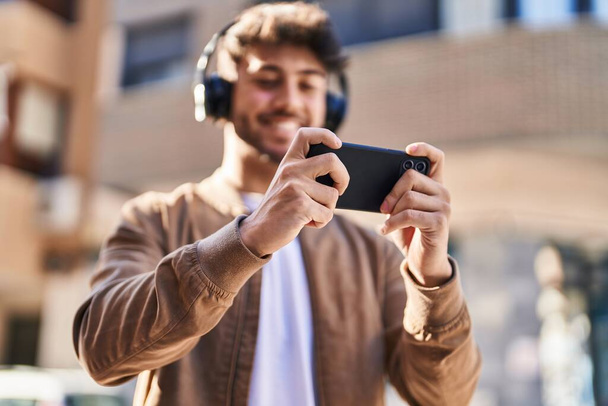 Молодий іспаномовний чоловік посміхається впевнено граючи відеоігри на вулиці
 - Фото, зображення