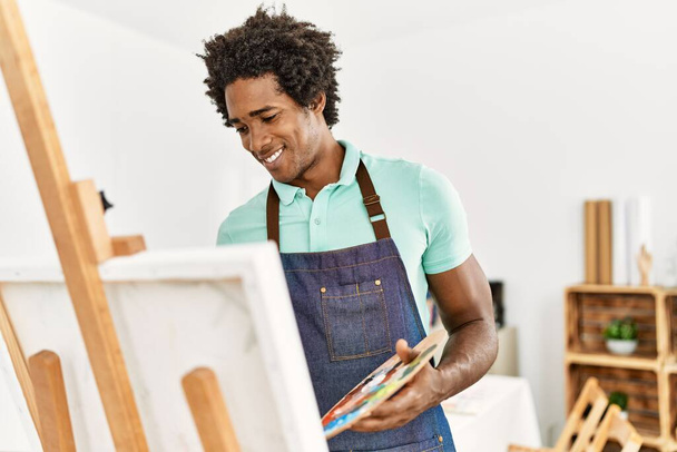 młody afrykański artysta amerykański człowiek uśmiecha szczęśliwy rysunek w studio sztuki. - Zdjęcie, obraz