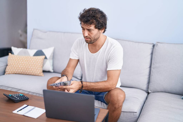 Young hispanic man using laptop accounting at home - 写真・画像