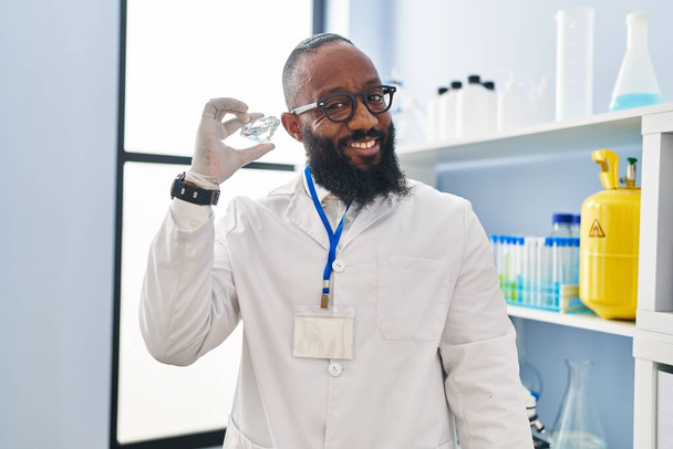 Joven afroamericano vistiendo uniforme científico sosteniendo diamante en laboratorio - Foto, Imagen