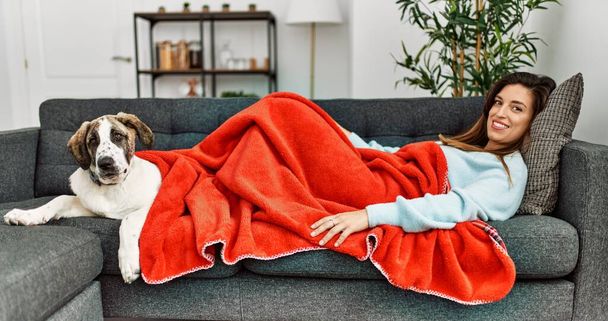 Giovane donna sorridente fiduciosa sdraiata sul divano con cane a casa - Foto, immagini