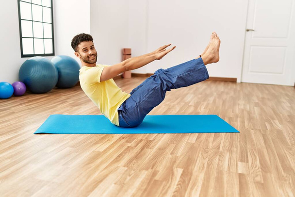 Giovane arabo sportivo uomo sorridente allenamento felice yoga al centro sportivo. - Foto, immagini