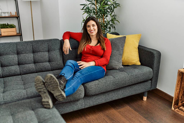 Молода жінка посміхається впевнено сидить на дивані вдома
 - Фото, зображення