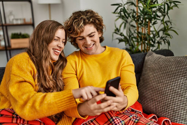 Junges kaukasisches Paar sitzt mit Smartphone zu Hause auf Sofa - Foto, Bild