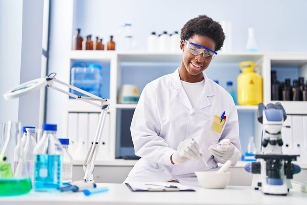 African american woman wearing scientist uniform working at laboratory - Фото, изображение