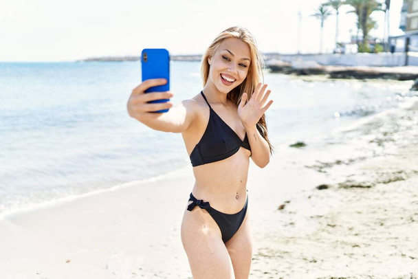 Young cuacasian girl wearing bikini having video call using smartphone at the beach. - Photo, Image