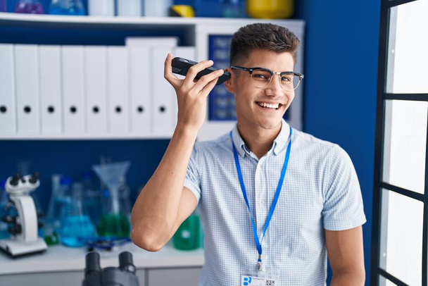 Młody latynoski naukowiec słuchający wiadomości audio przez smartfona pracującego w laboratorium - Zdjęcie, obraz