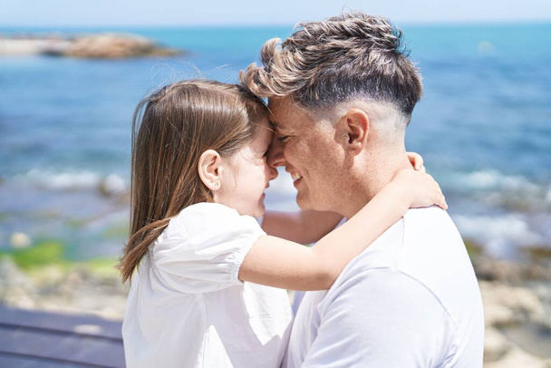 Padre e hija sonriendo confiados abrazándose en la orilla del mar - Foto, imagen