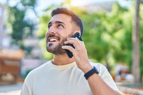 Молодий іспаномовний чоловік посміхається впевнено говорити на смартфоні в парку
 - Фото, зображення