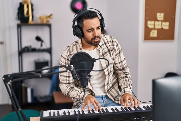Young hispanic man musician singing song playing piano keyboard at music studio - Φωτογραφία, εικόνα