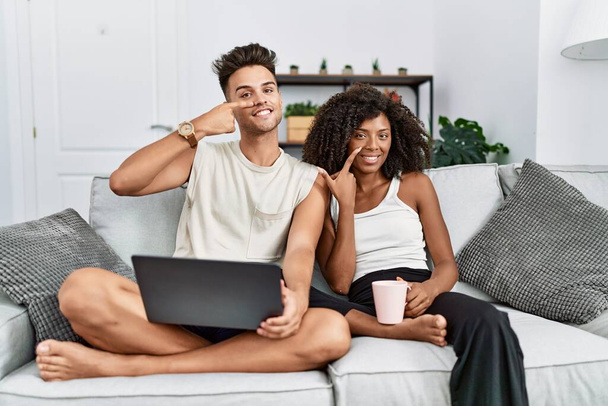 Genç bir çift evlerinde dizüstü bilgisayar kullanıyor kanepede oturuyor, elleri ve burunları birbirine dönük gülümsüyor. güzellik konsepti  - Fotoğraf, Görsel