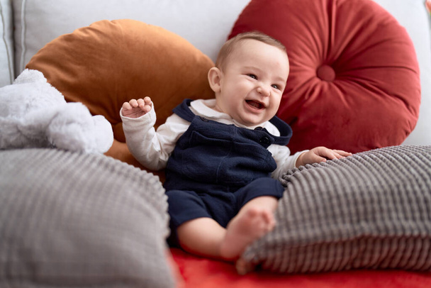 Adorable tout-petit souriant assis sur un canapé avec poupée de lapin à la maison - Photo, image