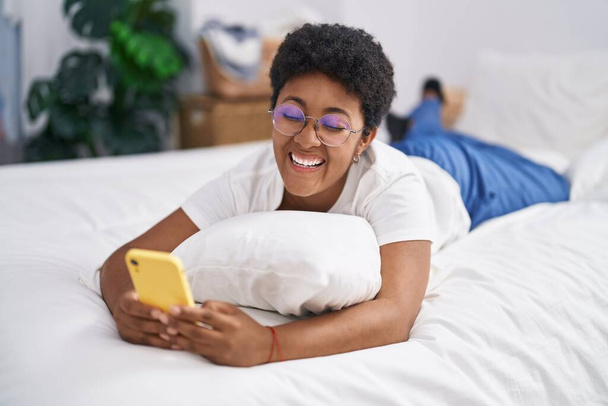 Afričanky americká žena pomocí smartphone ležící na posteli v ložnici - Fotografie, Obrázek