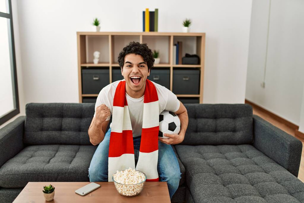 Fiatal spanyol férfi nézi foci mérkőzés és támogató csapat otthon. - Fotó, kép