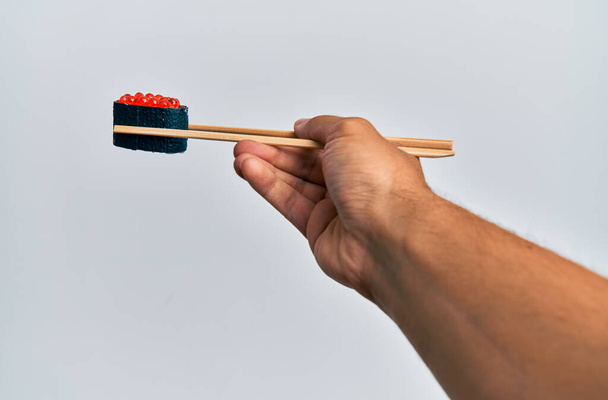  Hand of man holding salmon roe sushi with chopsticks over isolated white background - Фото, зображення
