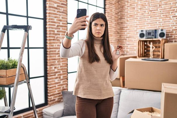 Fiatal barna nő költözik egy új otthon csinál video hívás szkeptikus és ideges, homlokráncolás ideges, mert a probléma. negatív személy.  - Fotó, kép
