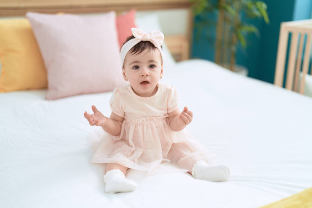 Adorable toddler sitting on bed with relaxed expression at bedroom - Foto, Imagen