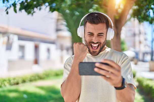 Junger hispanischer Mann lächelt selbstbewusst Videospiel im Park - Foto, Bild